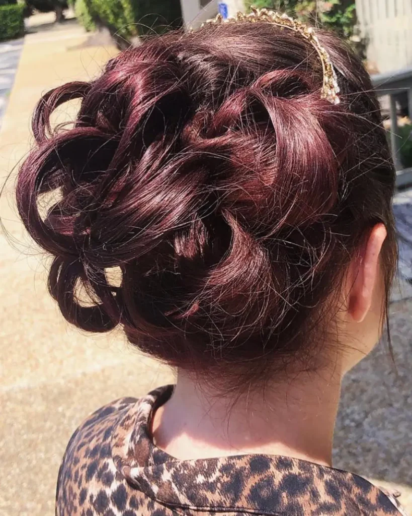 Woman with dark maroon hair styled in an intricate, curly updo, wearing a gold headband and a leopard print top, photographed from behind outdoors. - Fringe Salon, Hiltonhead, SC