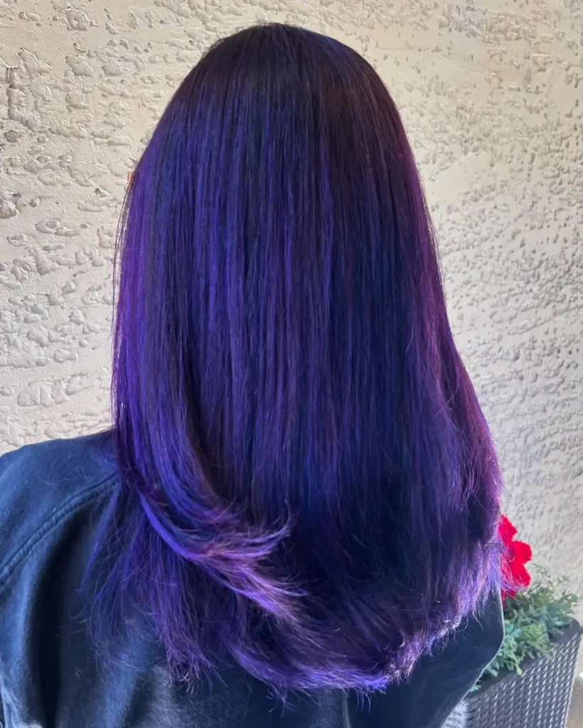 Person with straight, shoulder-length hair dyed a vibrant purple, photographed from behind against a textured light-colored wall. - Fringe Salon, Hiltonhead, SC